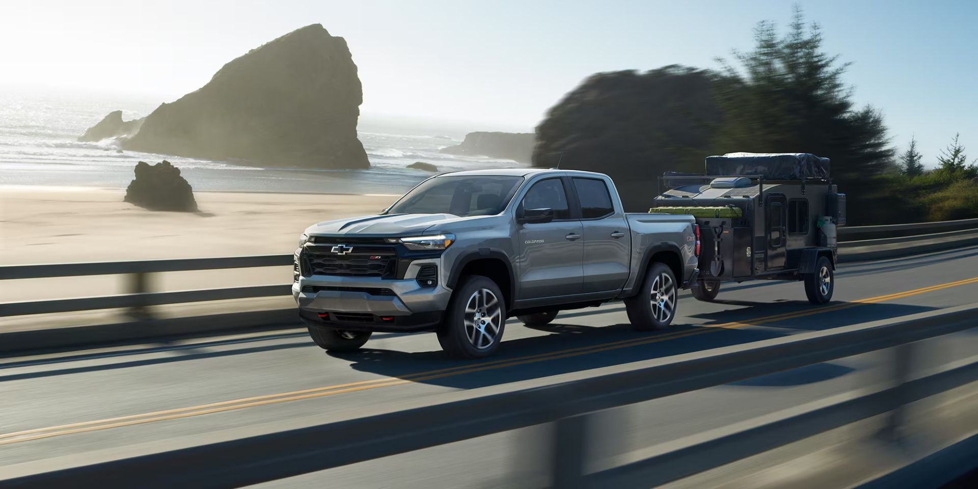 A silver truck pulling a trailer on the road.