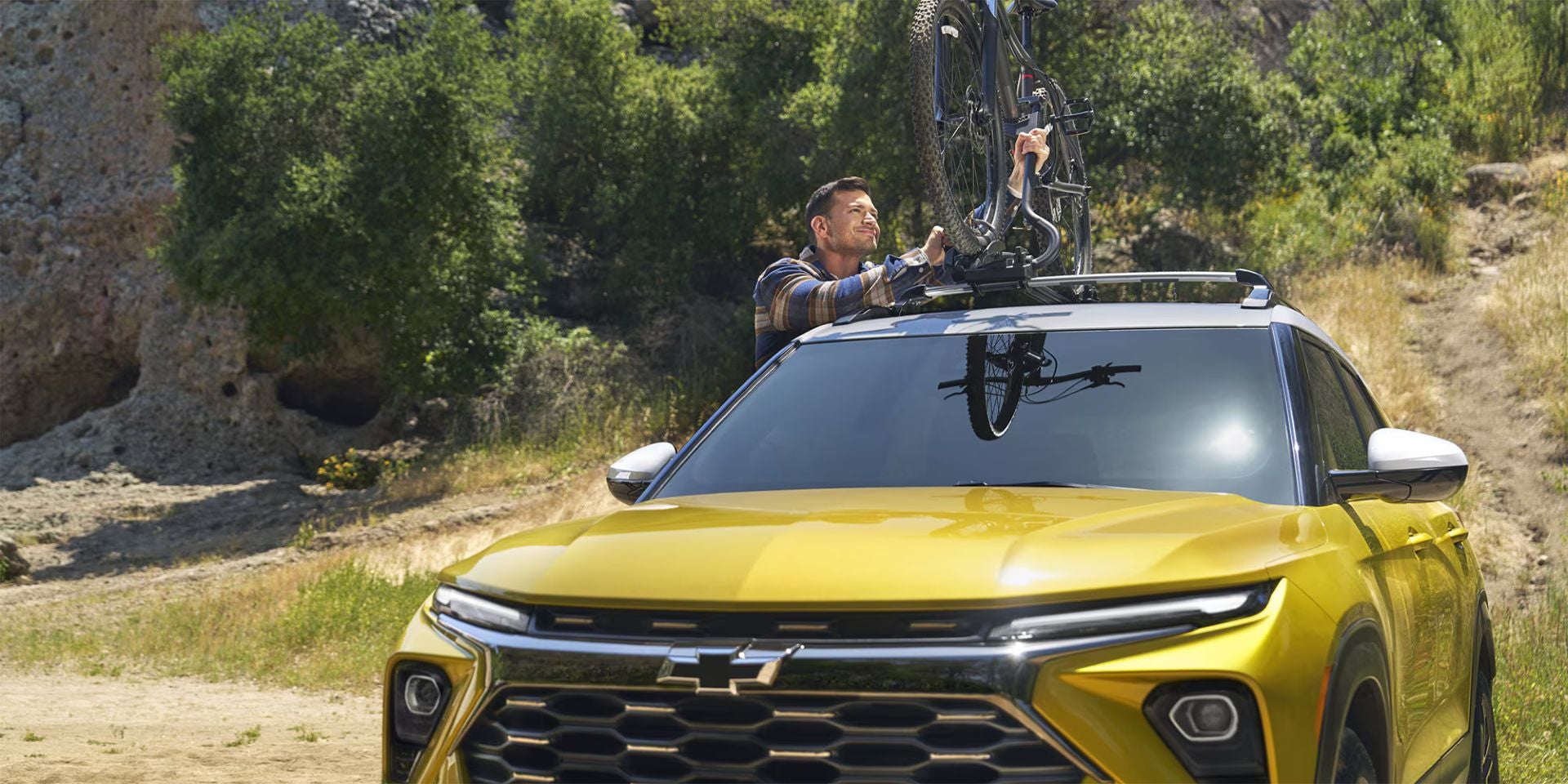 A man putting a bike on top of a yellow suv.